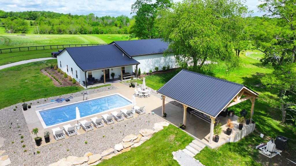 tranquil home with a striking black metal roof, white siding, a pool, and pavilion