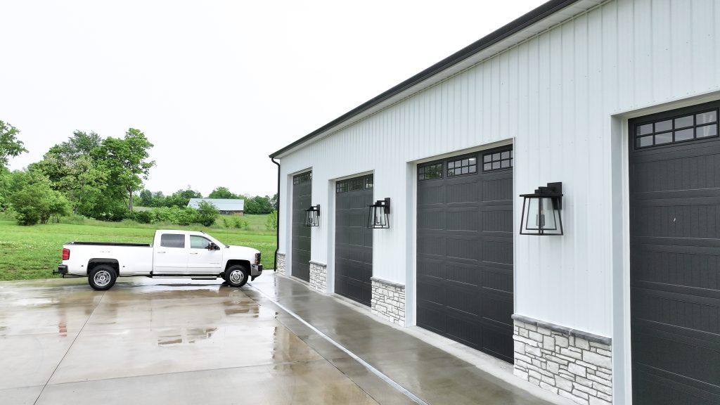 White metal panels are used as siding with black garage doors installed on this catchy garage